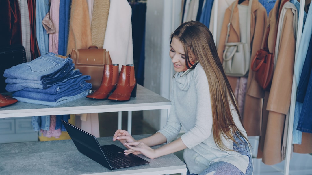 Woman working on a laptop surrounded by clothes.
