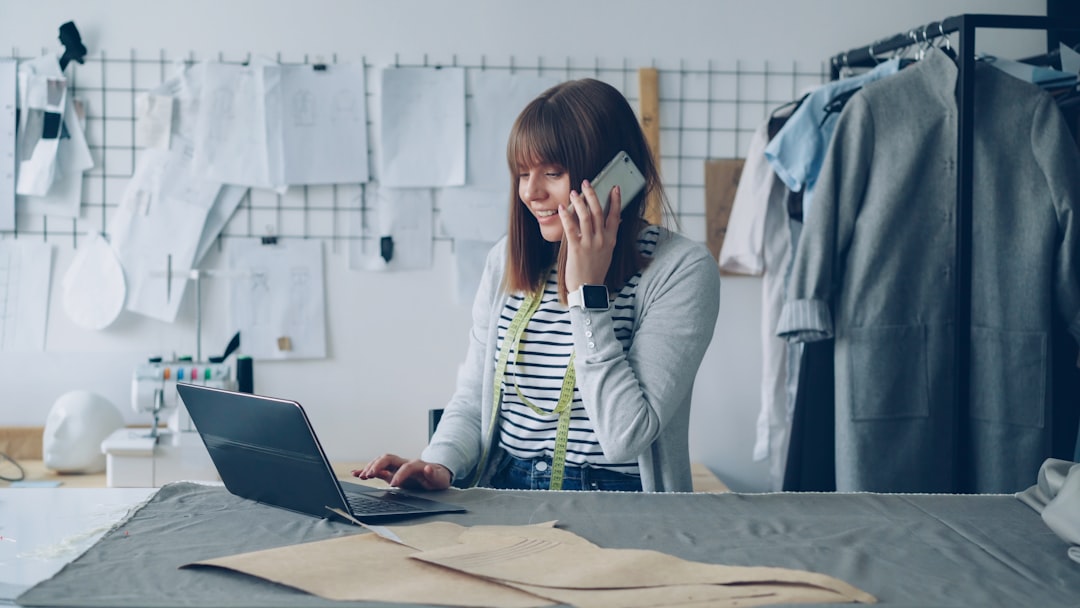 Fashion designer works on laptop while talking on phone.