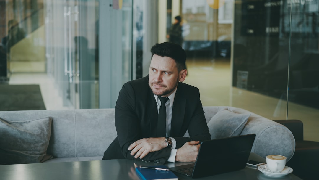 Man in suit sitting at table with laptop and coffee.